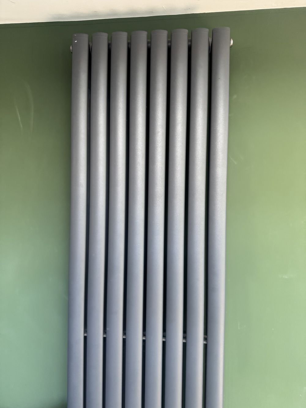 Anthracite designer column radiator on a green wall